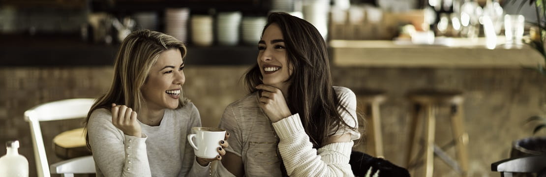 Two women smile and laugh while sitting in a cafe